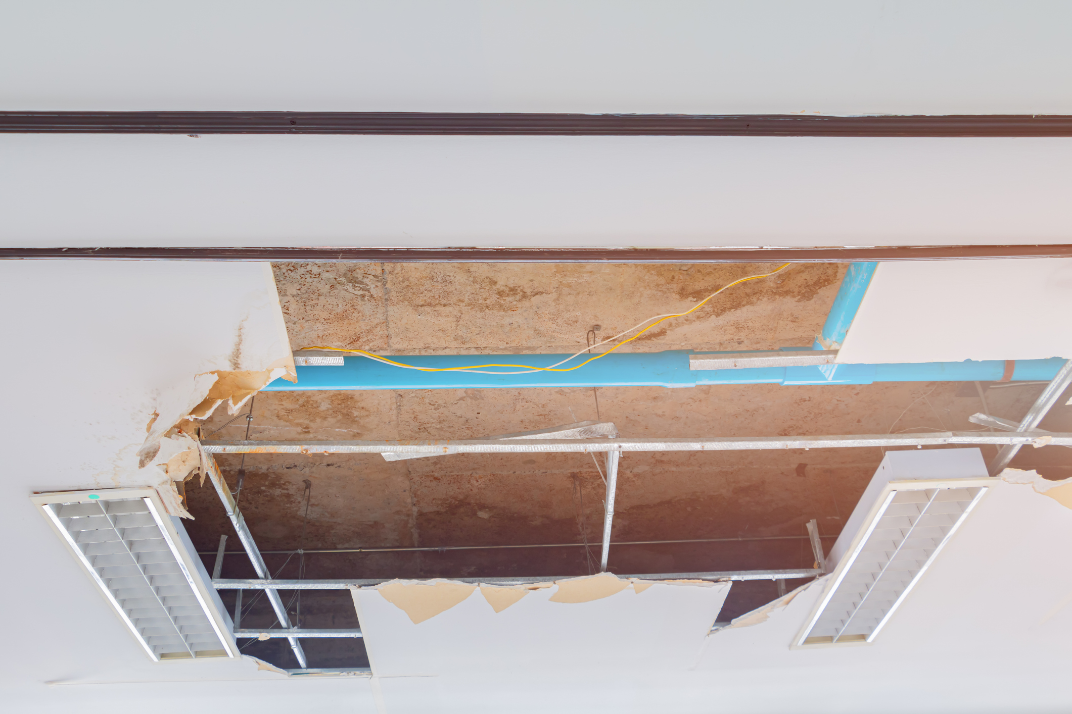 Commercial ceiling damage from water leak showing exposed pipes and infrastructure