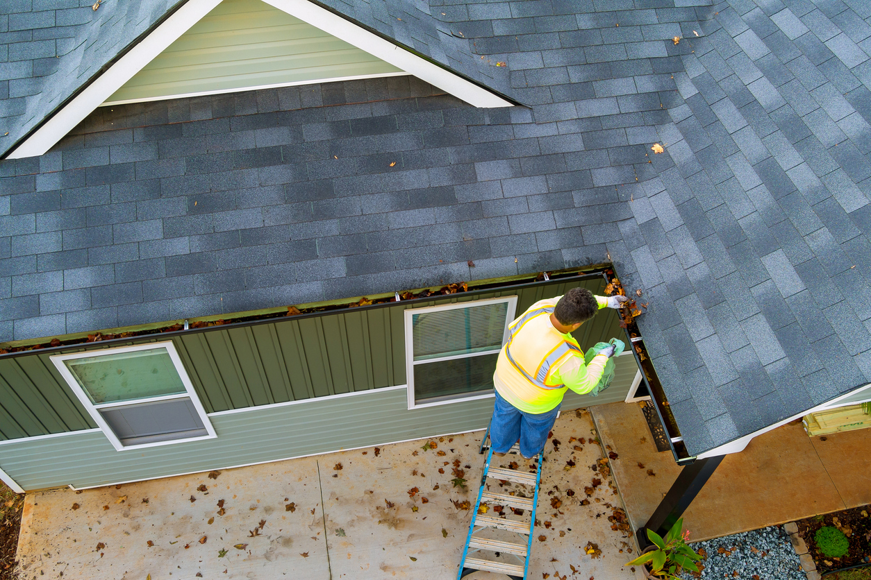 Homeowner cleaning gutters for summer storm preparation